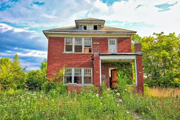 A red brick house with a porch and a green field.