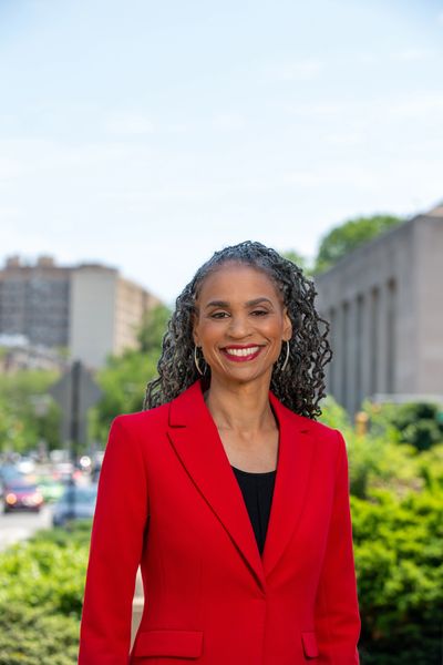 A woman in red jacket standing on street next to trees.