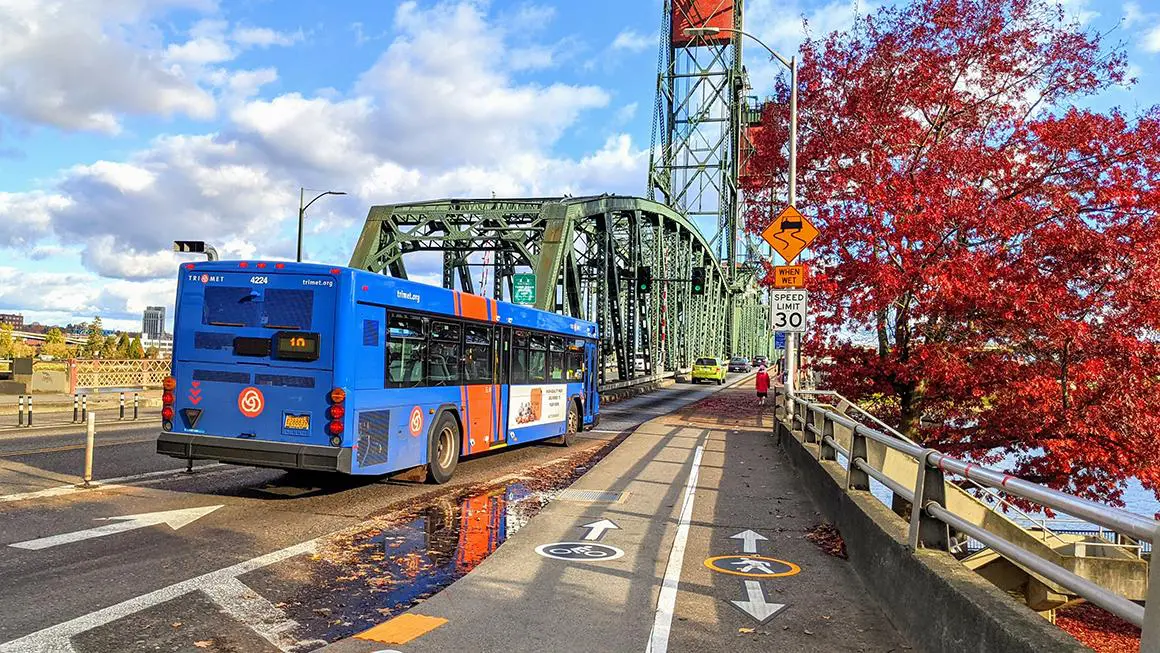 A blue bus driving down the street near a bridge.